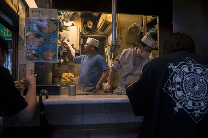 Two chefs working in a small, bustling kitchen in Japan, perfect for urban street photographers.