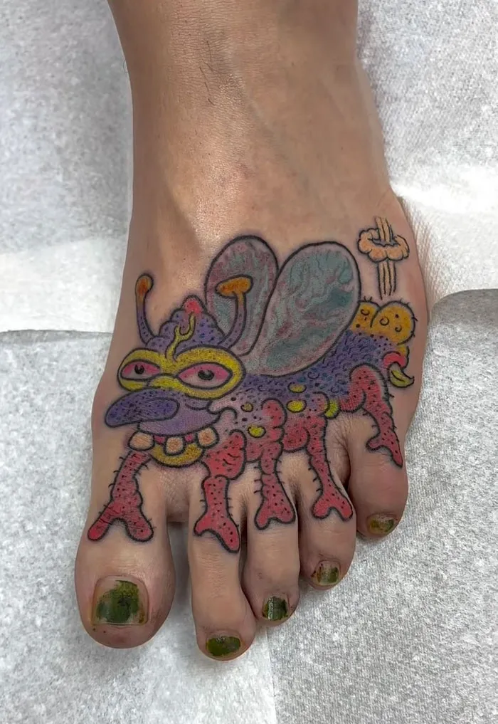 A tattoo artist's talent is displayed on a foot with a colorful cartoon bug tattoo, a questionable idea.