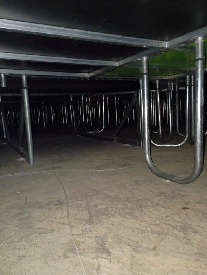 An unsettling view beneath a stage structure, revealing a hidden, dark liminal spaces with metal supports and wires.