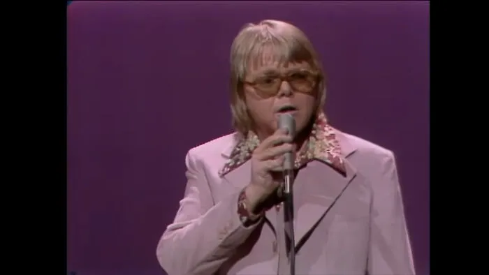 A male singer with a microphone and sunglasses performing on stage, taking you way back and reminding you how old you are.