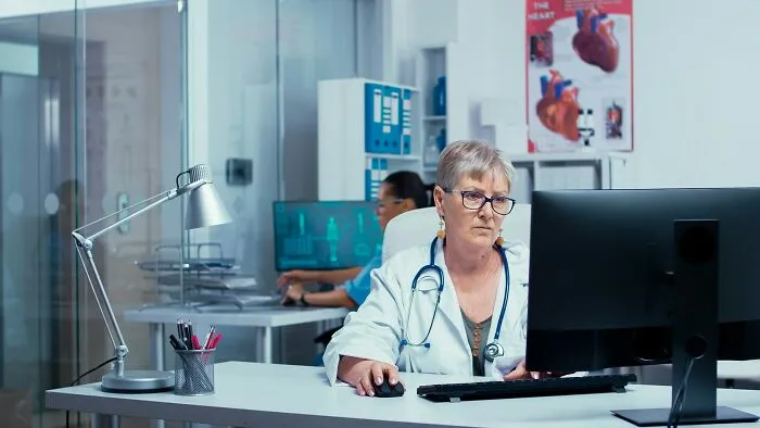A female doctor works at a computer in a clinic, managing health trends and patient care to prevent intense stress and burnout.