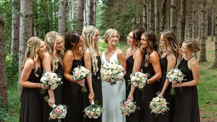 Bride surrounded by bridesmaids holding bouquets in a forest wedding setting