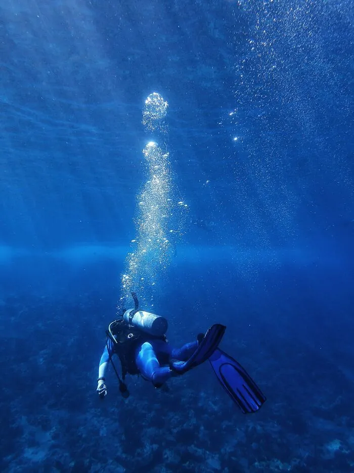 Scuba diver ascending with bubbles underwater clear blue water diving story