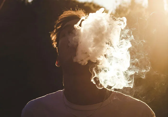 Person exhaling thick vapor smoke outdoors at sunset