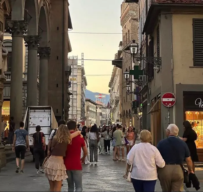 A couple walking down a busy European street with their arms around each other, a wholesome photo trend.