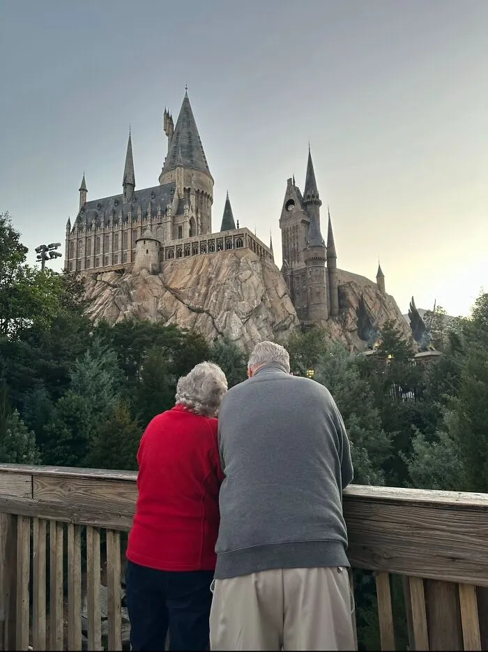 An elderly couple stands with their backs to the camera, looking at the Hogwarts castle, captured in a wholesome photo trend.