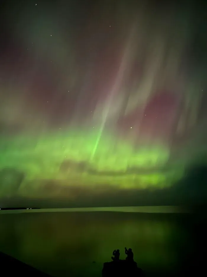 Silhouettes of strangers against an aurora, showcasing the wholesome photo trend.