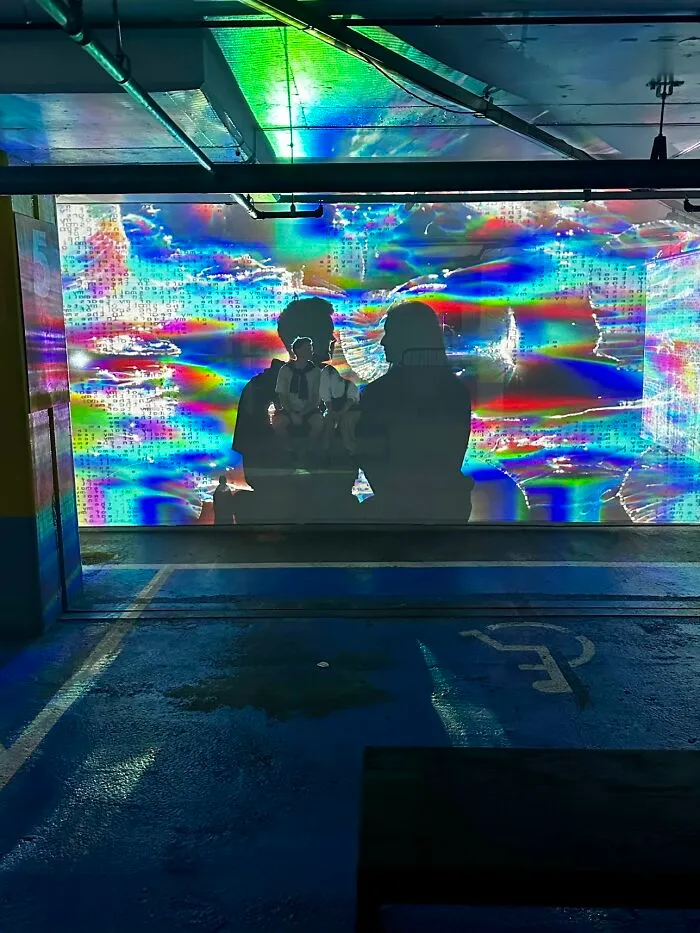 A vibrant photo trend capturing two silhouettes against a colorful, abstract light display in a parking garage.