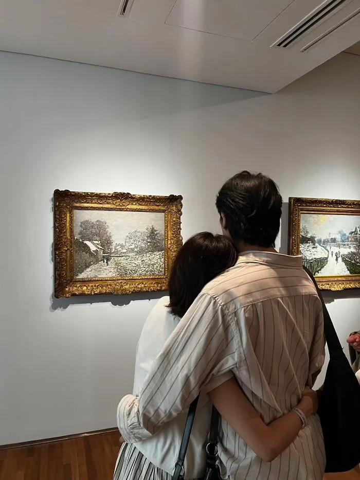 A couple from behind, embracing while looking at paintings in a museum, like a painting, wholesome photo trend.