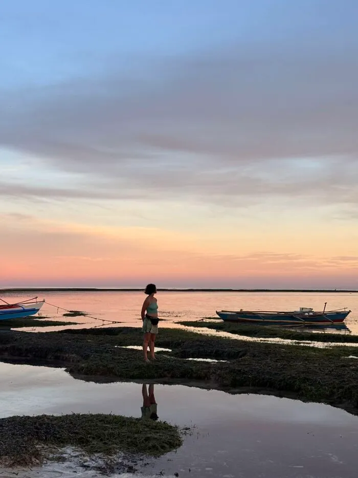 A wholesome photo trend of a woman at sunset by the water with boats, like a painting.