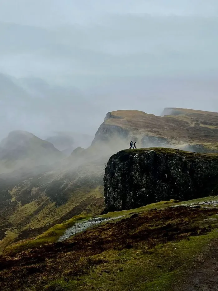 A wholesome photo trend of two strangers on a misty cliffside, resembling a painting.