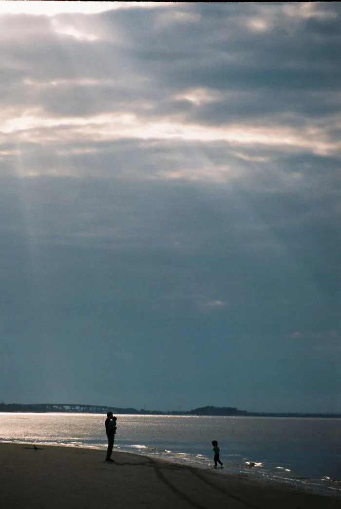 Silhouettes of a parent and child on a beach under a dramatic sky, a wholesome painting photo trend.