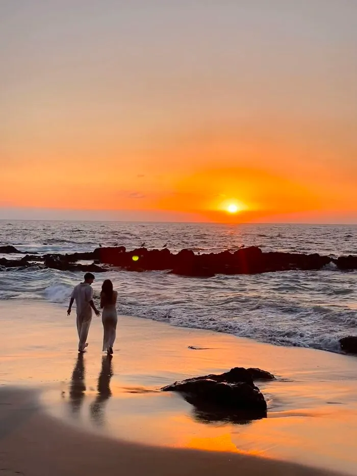 A couple walks along a beach at sunset, a wholesome photo trend of beautiful moments.