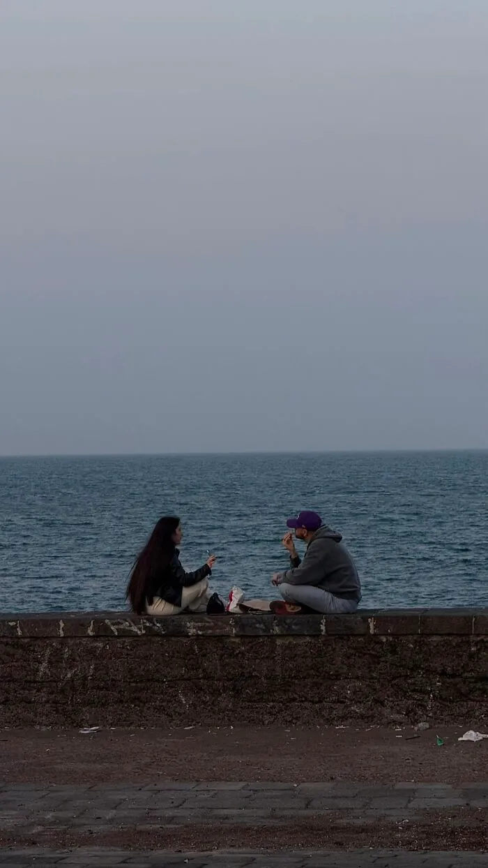 A couple sits on a sea wall enjoying the view, capturing the wholesome photo trend.