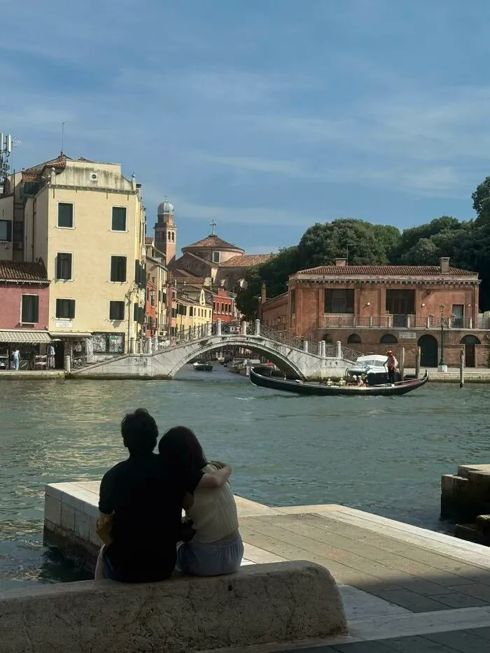 A wholesome photo of a couple embracing by a canal in Venice, embodying the 'Like A Painting' photo trend.