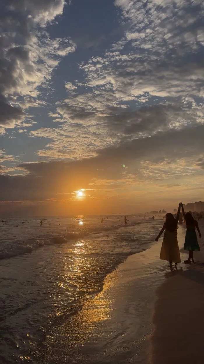 A wholesome photo of two people holding hands on a beach at sunset, reflecting the beautiful photo trend.