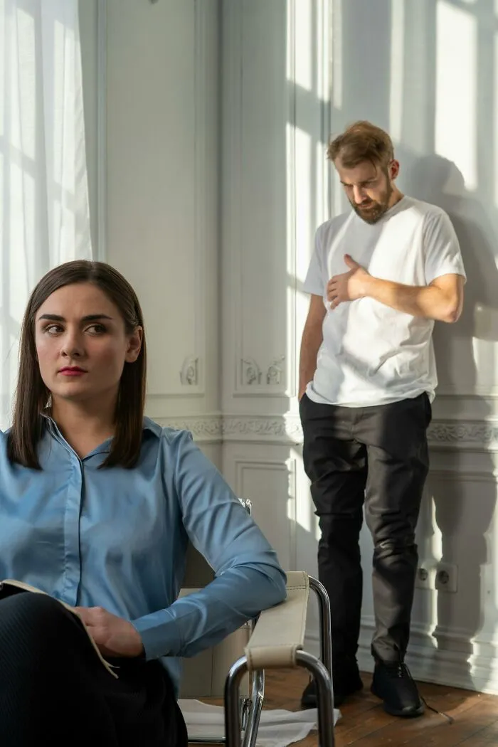 Woman looking away while man stands in sunlight in tense room