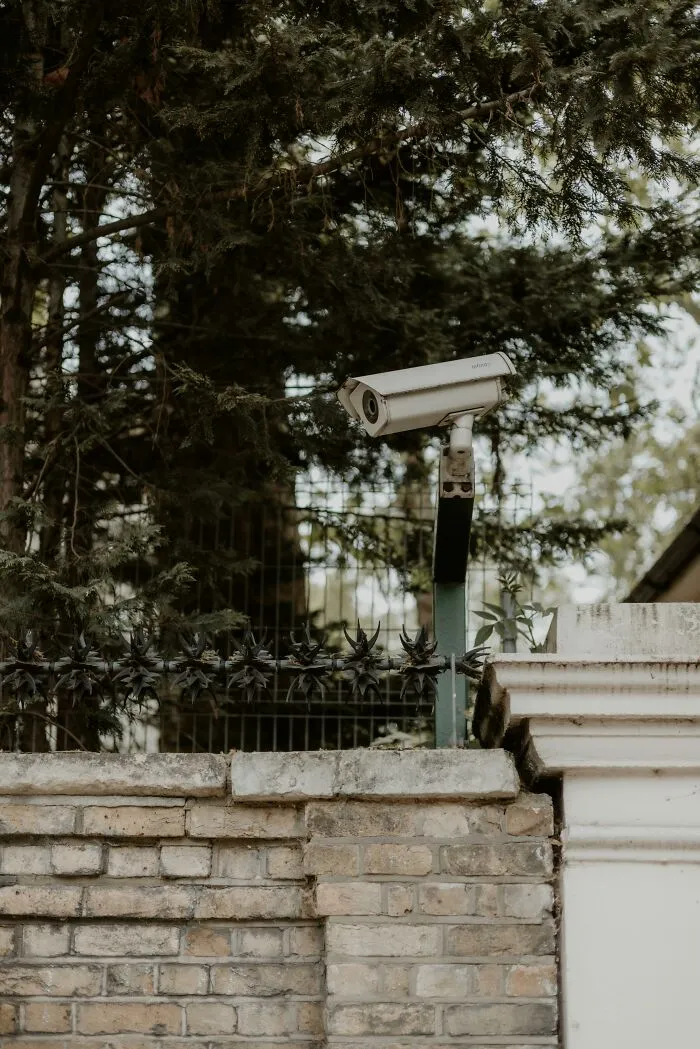 Security camera mounted on brick wall near trees