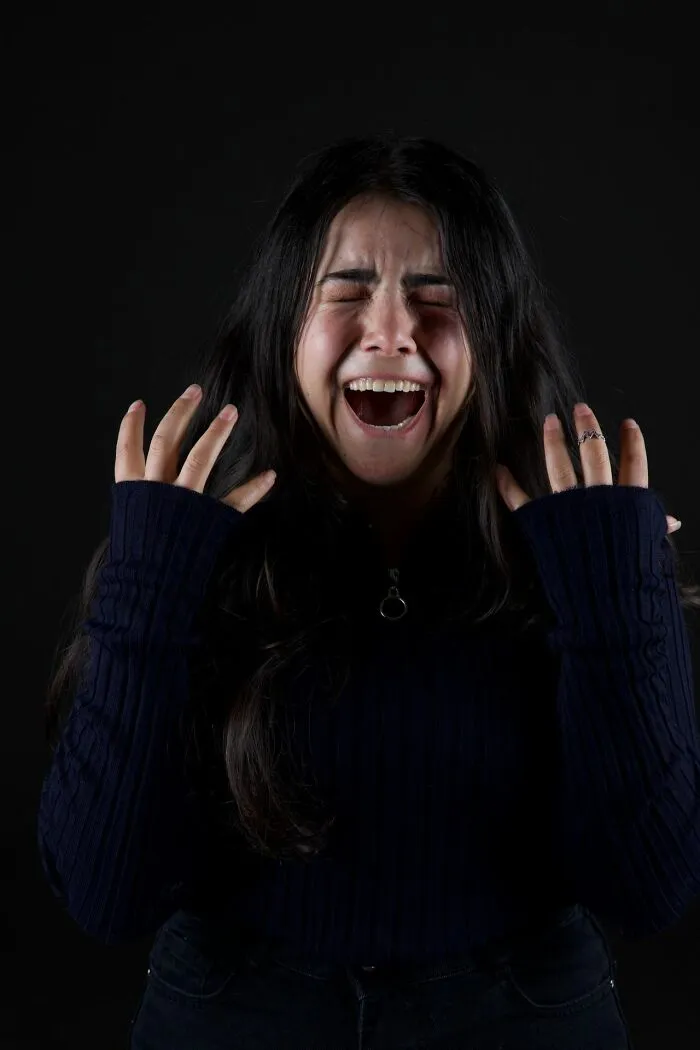 Person screaming with eyes closed and hands raised on black background