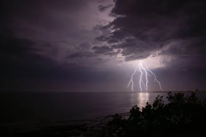 Lightning storm over ocean at night with dark clouds diving story