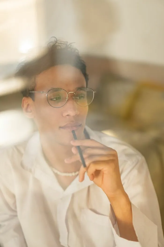 A pensive man in glasses holding a pen to his lips, revealing hints of a person who is secretly very smart.