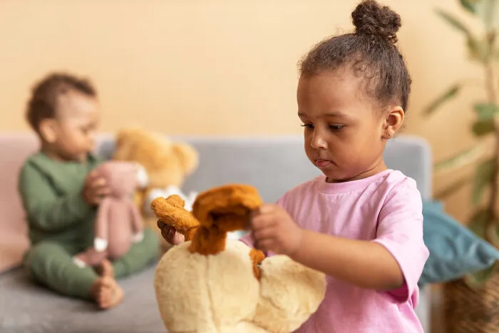 Primary girl playing with teddy bear showing troubling behavior
