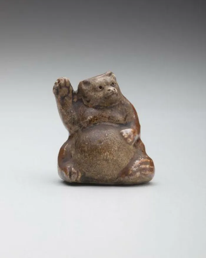 Intact after years, a small, brown, ceramic animal figurine with one paw raised, resembling a beckoning creature.