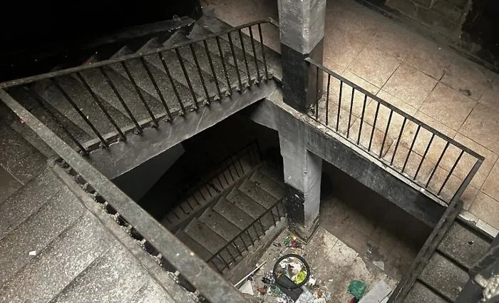 A dark, dirty, multi-level concrete staircase with debris, showcasing unhinged real estate listings.
