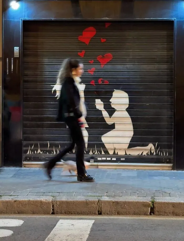 Divertida foto accidental de una mujer caminando frente a un grafiti de propuesta de matrimonio con corazones rojos.