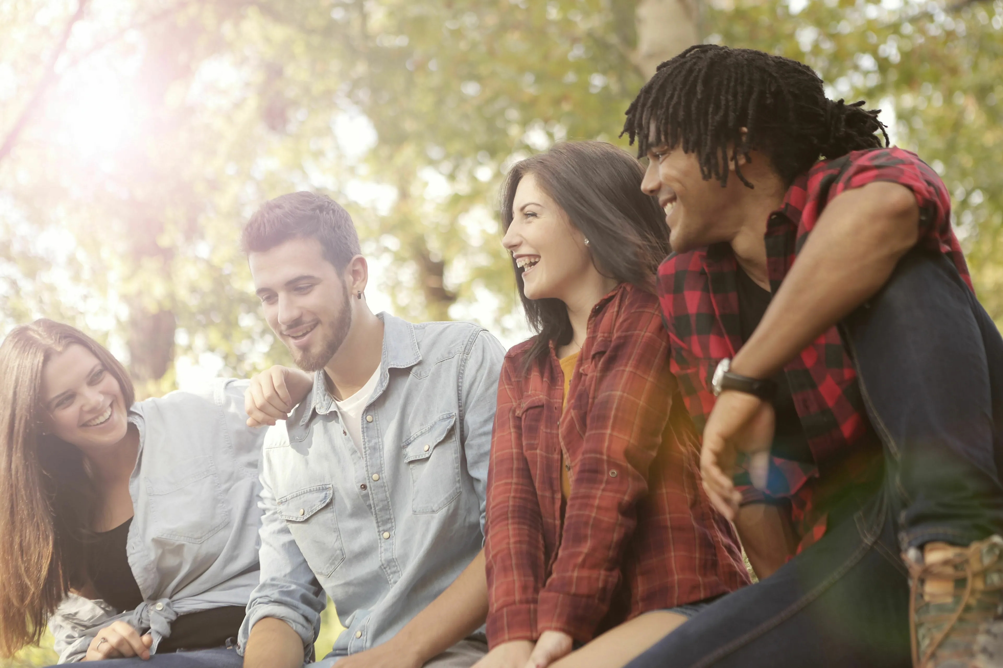 Four diverse young adults smiling and laughing together outdoors, illustrating different types of friendship.