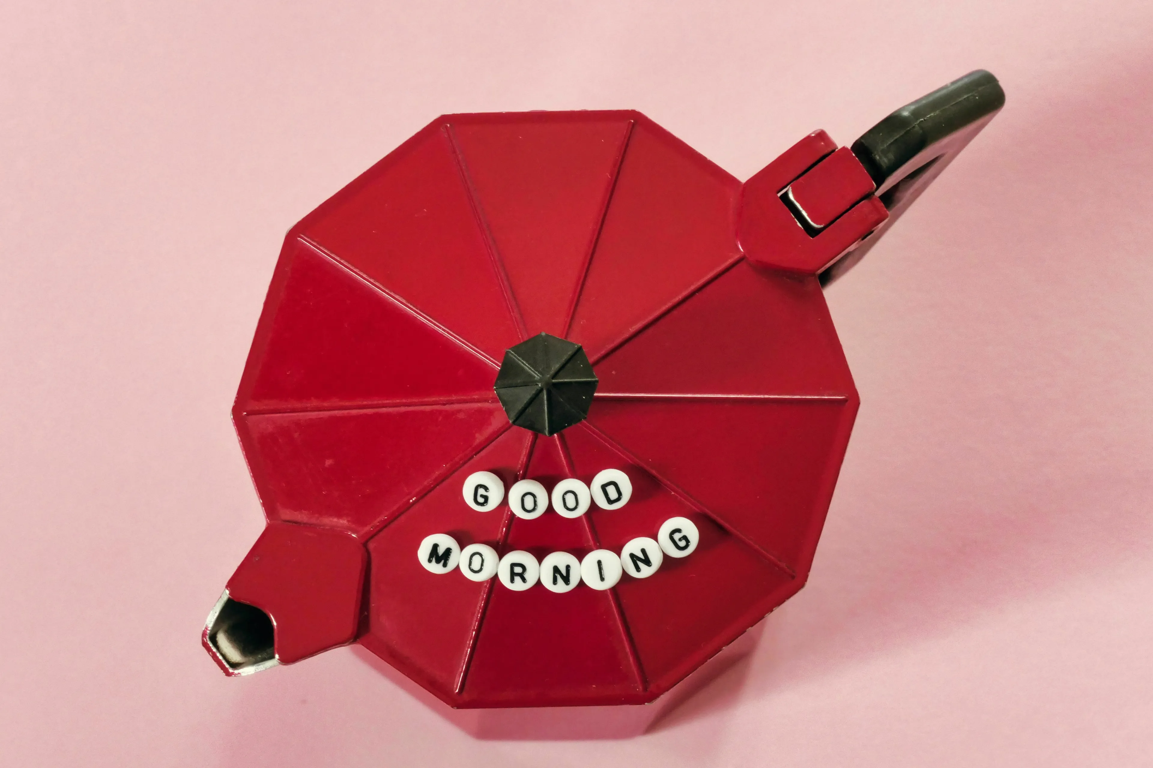 A red coffee pot with 'Good Morning' spelled out in beads on top, representing a morning routine before a big day.