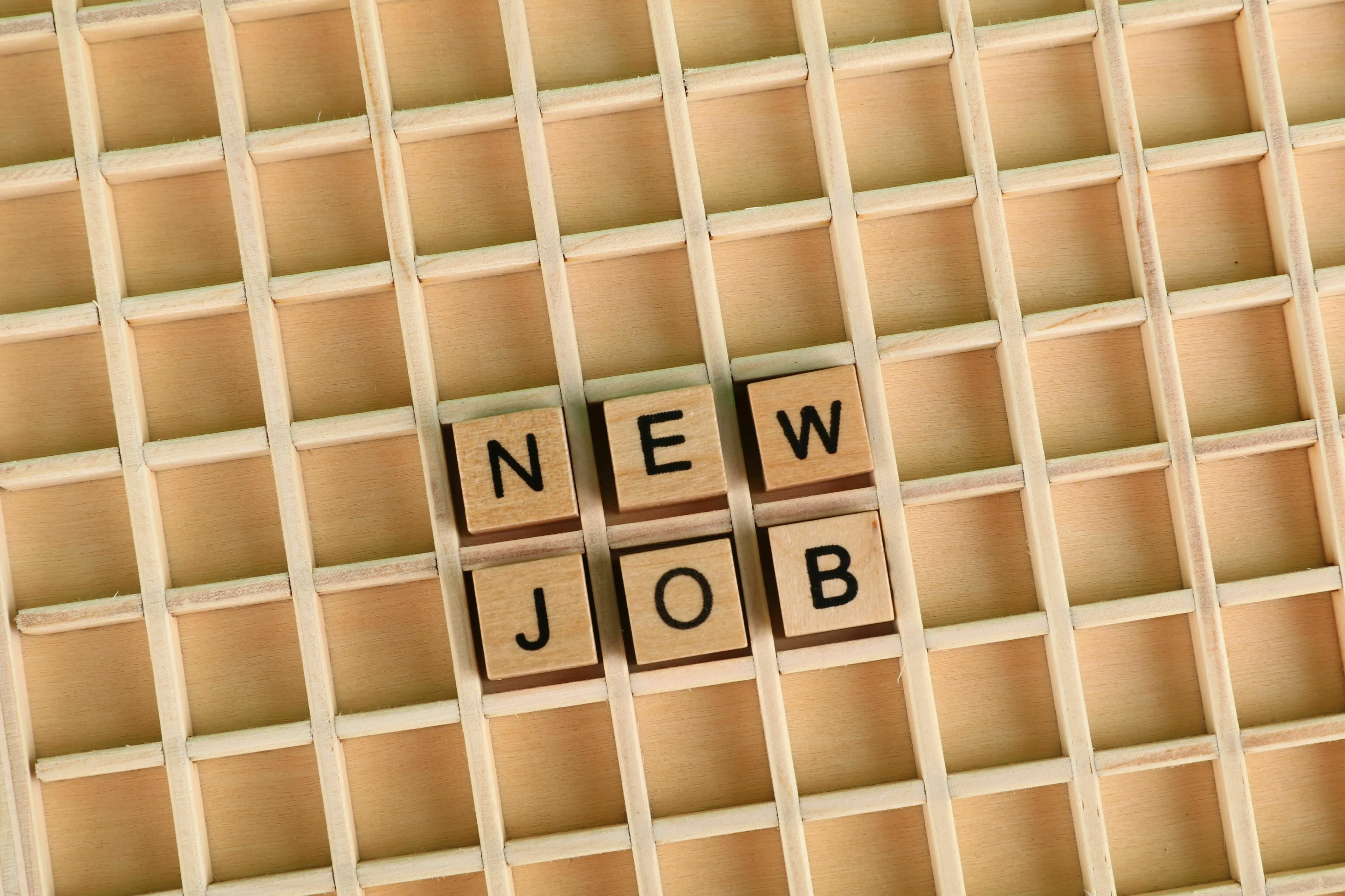 Wooden letter tiles spelling out NEW JOB arranged on a grid, representing a career change and risk-taking.