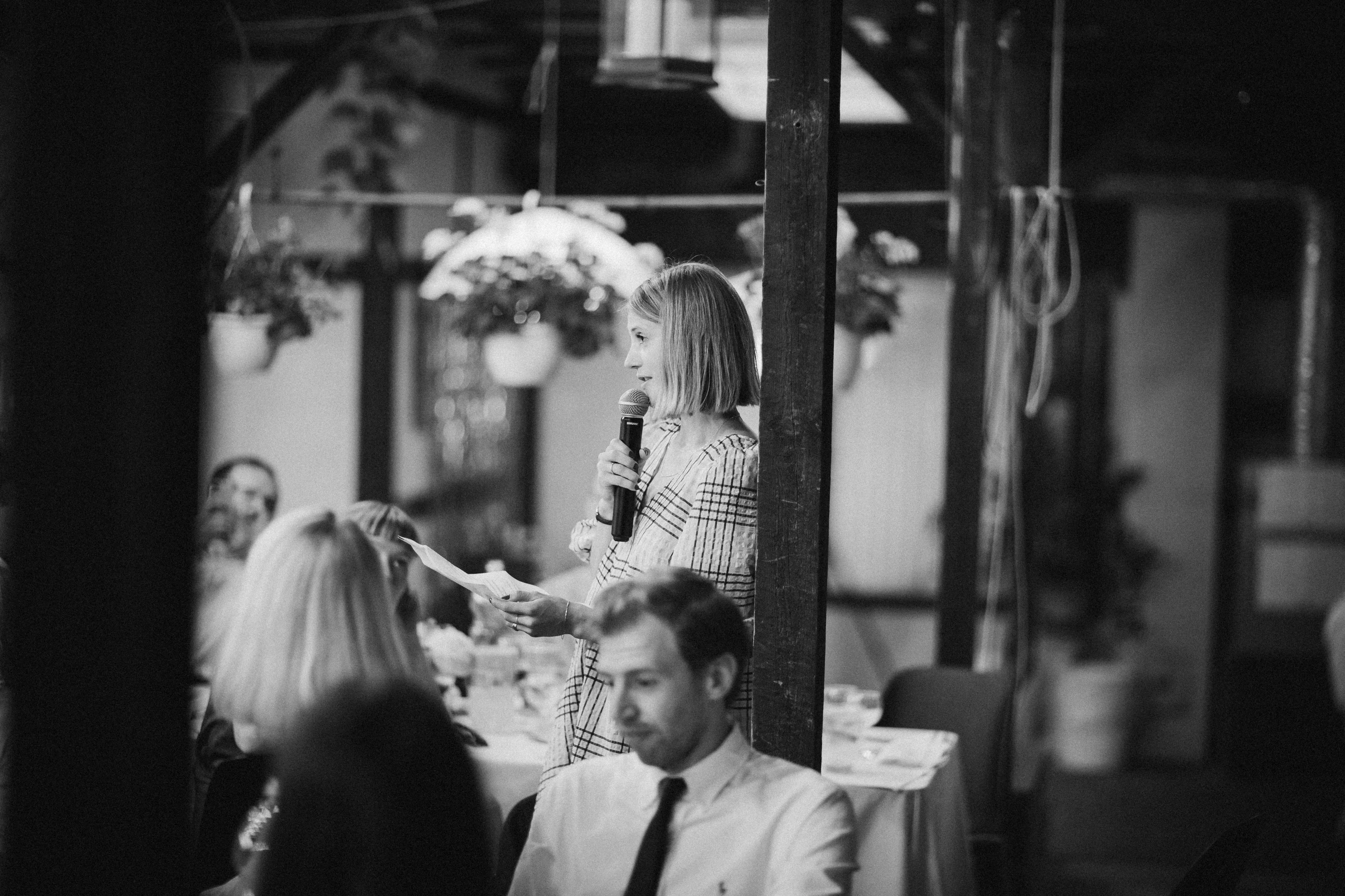 A woman holds a microphone and a piece of paper, speaking at a wedding, illustrating risk taker behavior.
