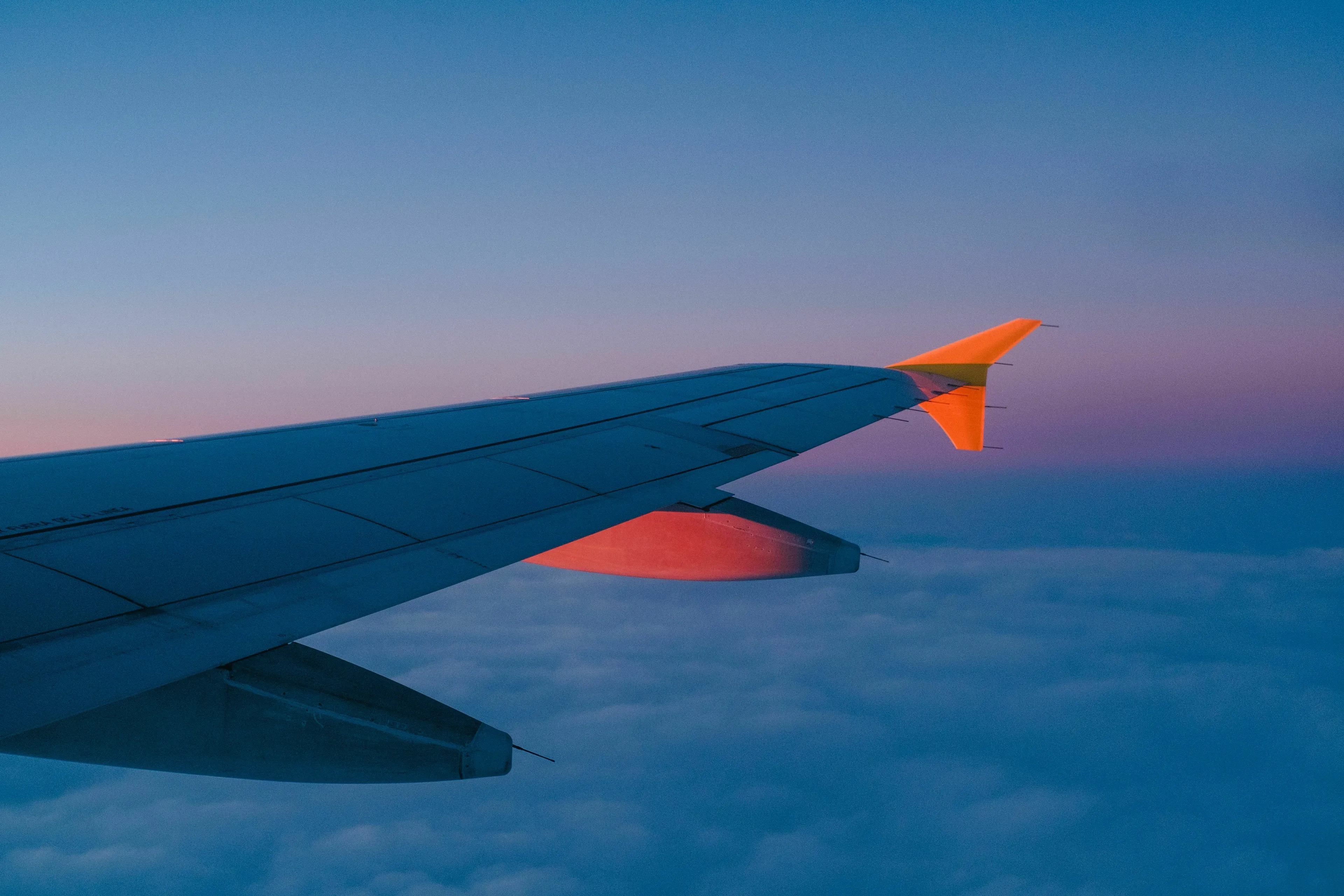 An airplane wing against a twilight sky with clouds below, symbolizing a flight canceled scenario for a risk taker.