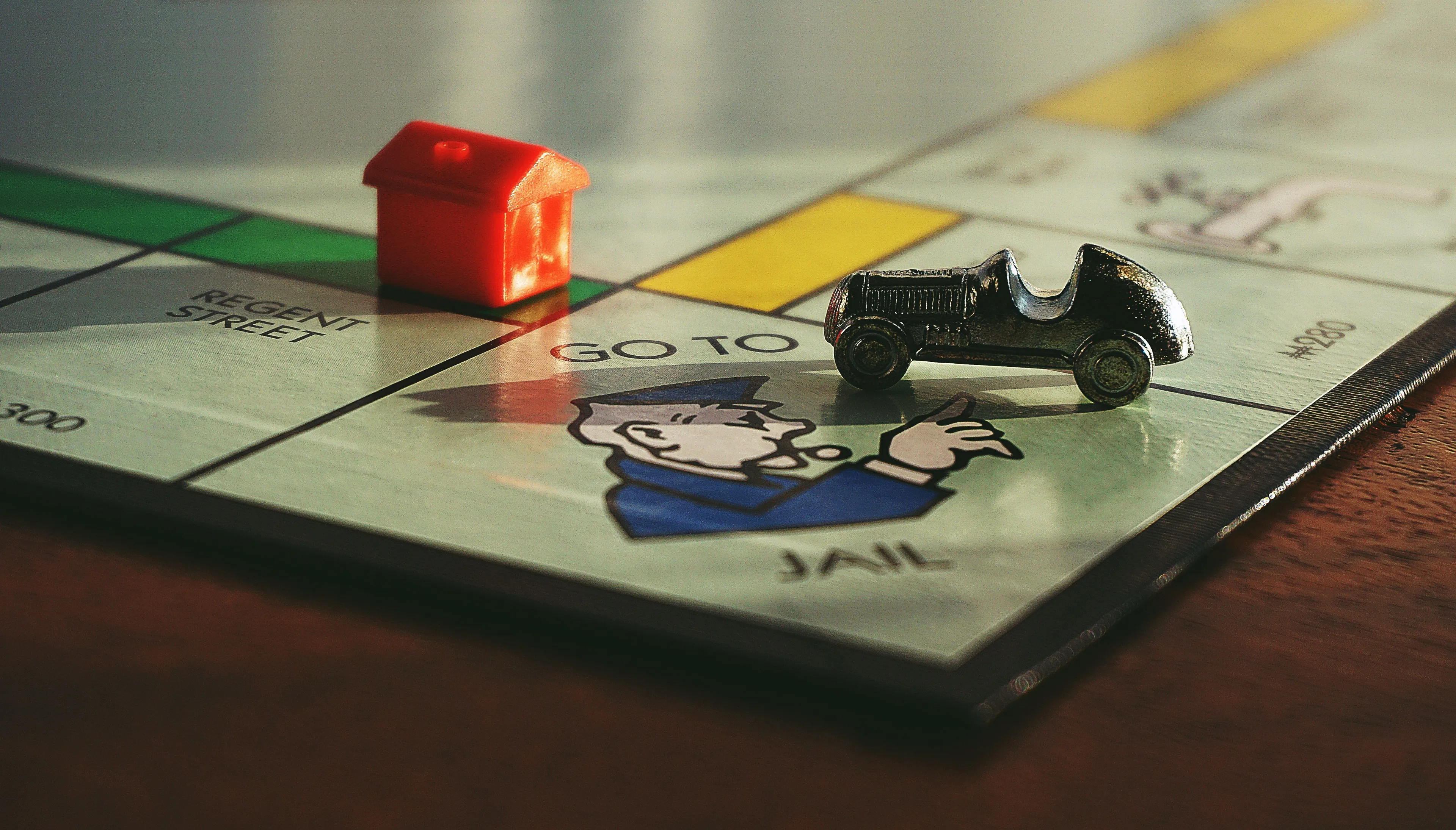 A Monopoly board game with a red house and a silver car token near the GO TO JAIL space.