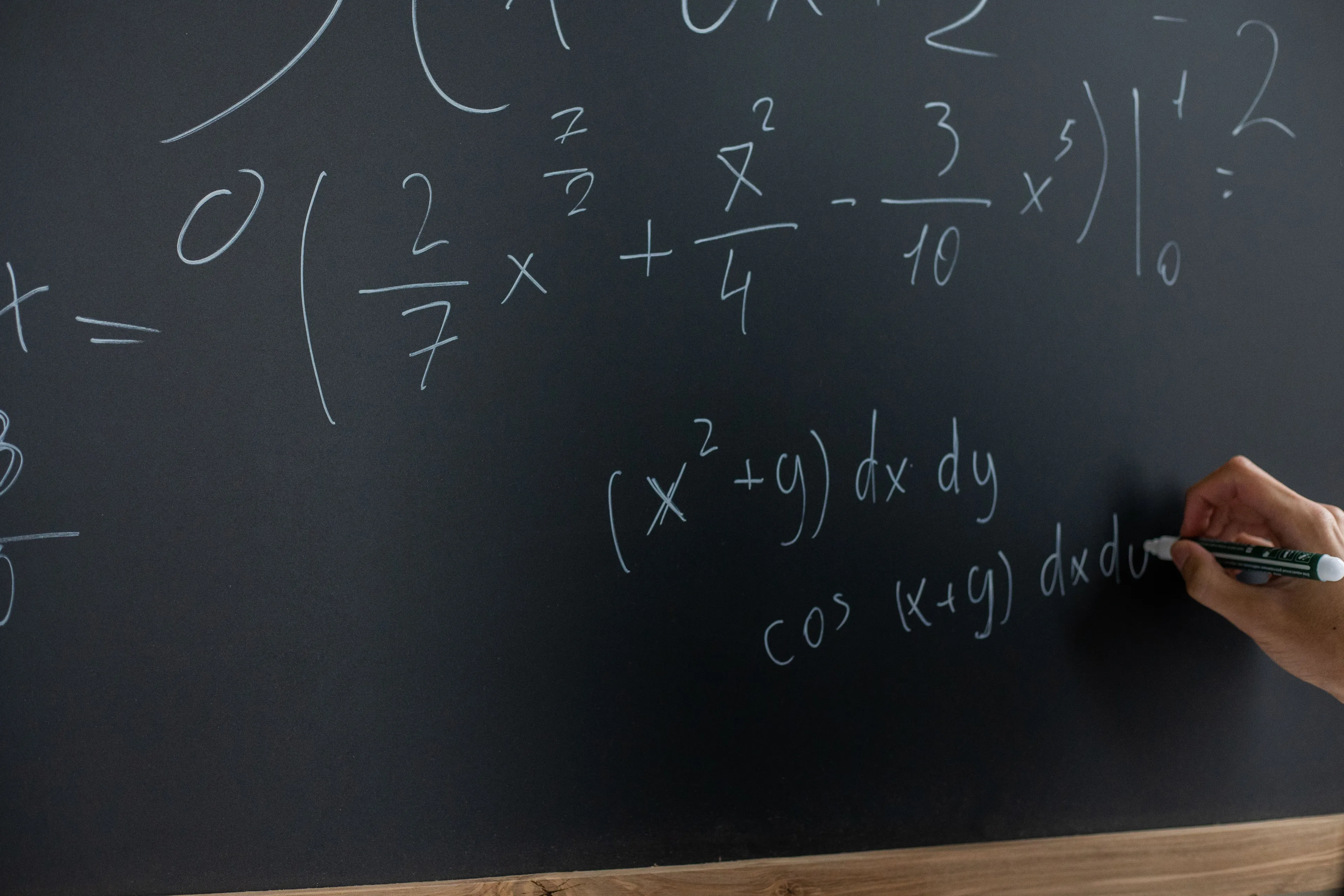 A hand writing complex math equations on a blackboard, highlighting the Maths subject.