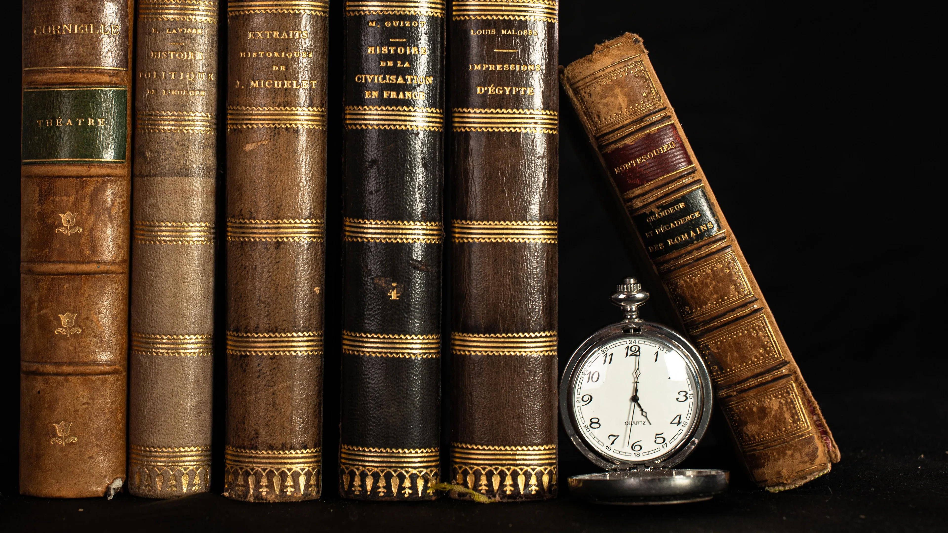 A collection of old, leather-bound books and a pocket watch, symbolizing the school subject of History.