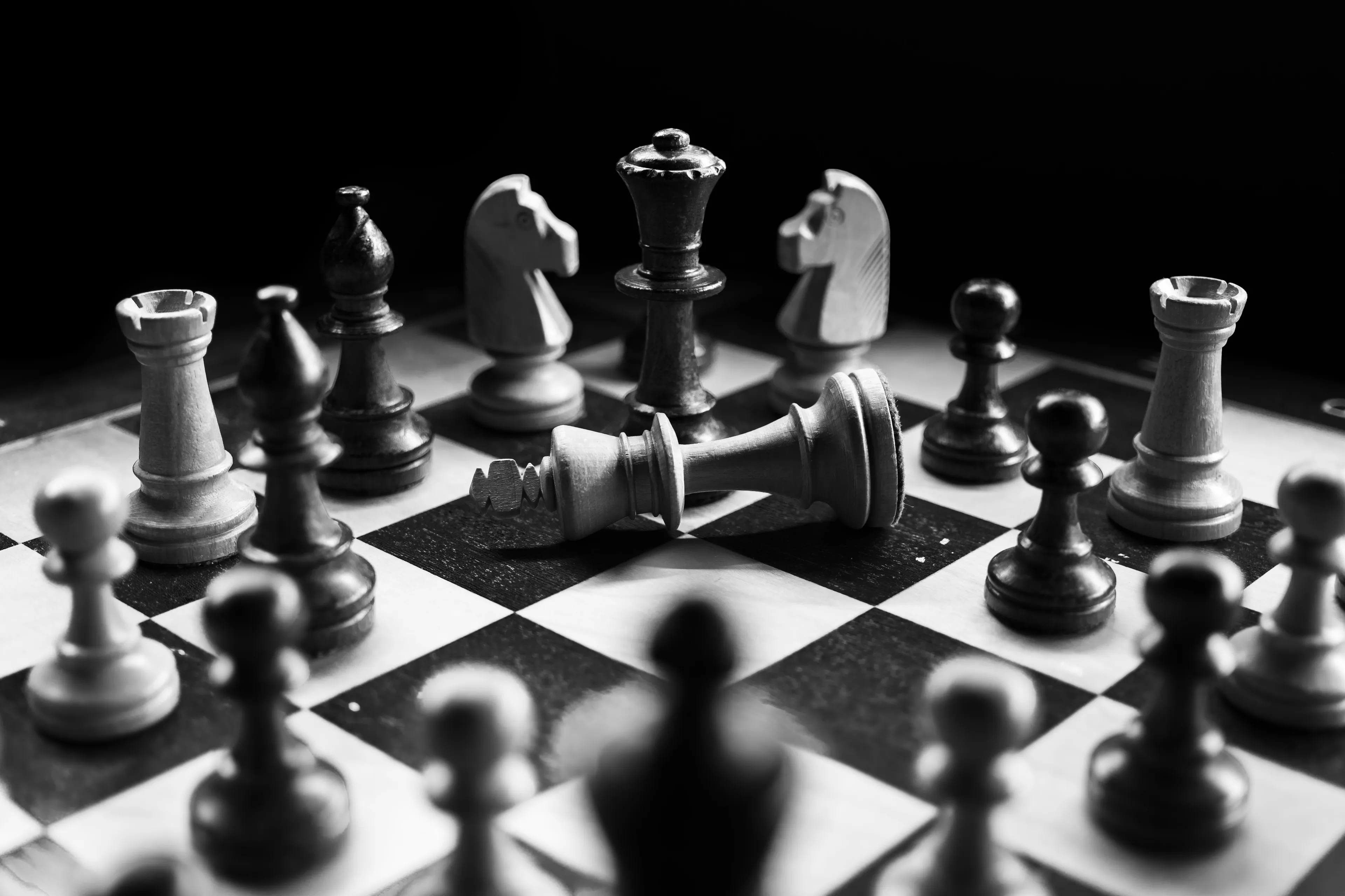 A black and white close-up of a chessboard with pieces arranged, including a fallen king, highlighting the game of chess.