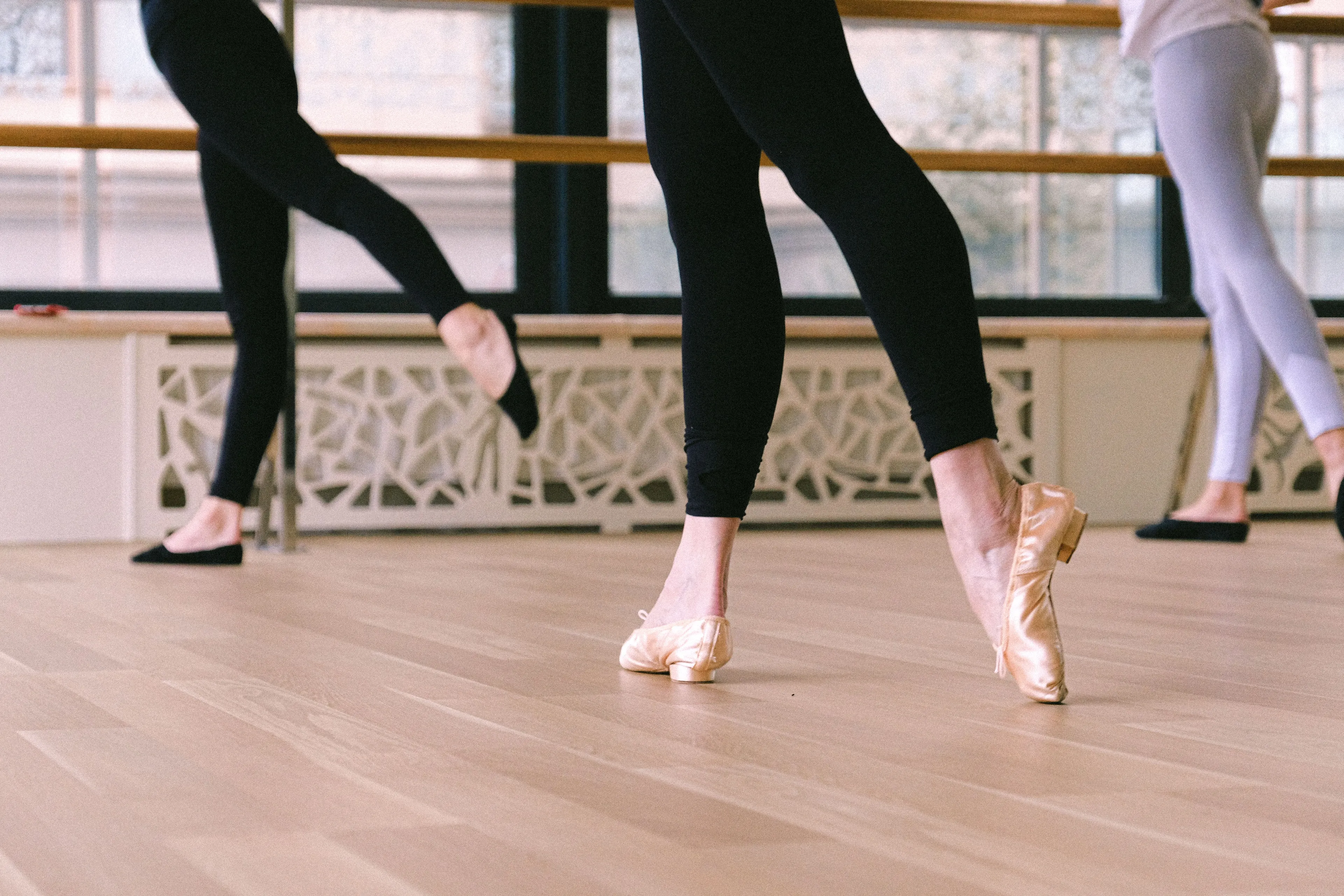 Multiple people in dance class, wearing leotards and ballet shoes, with one person in focus on their toes during dance classes.