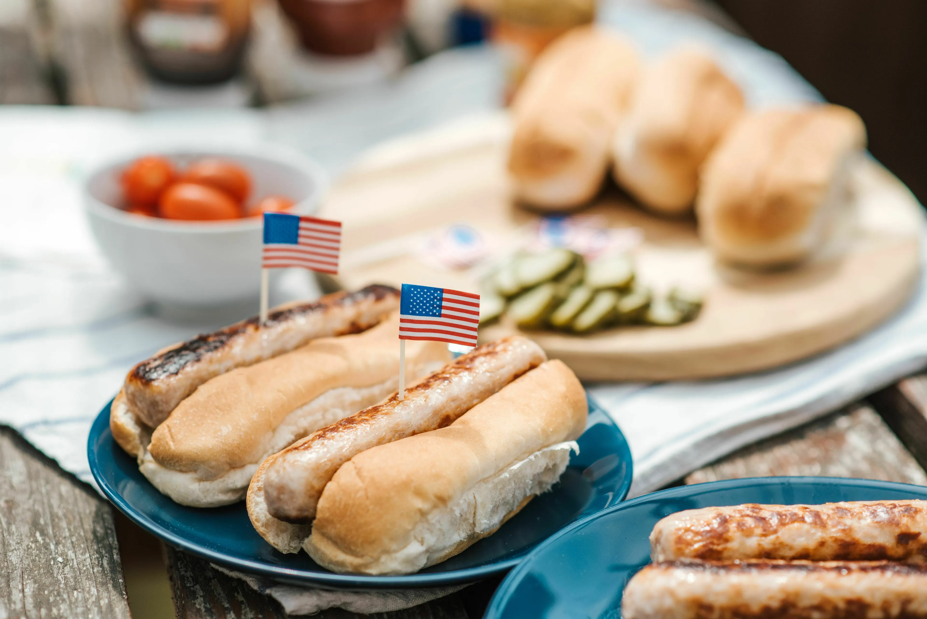 Hot dogs with American flags on a picnic table, representing the numerous hot dogs Americans eat on Fourth of July.
