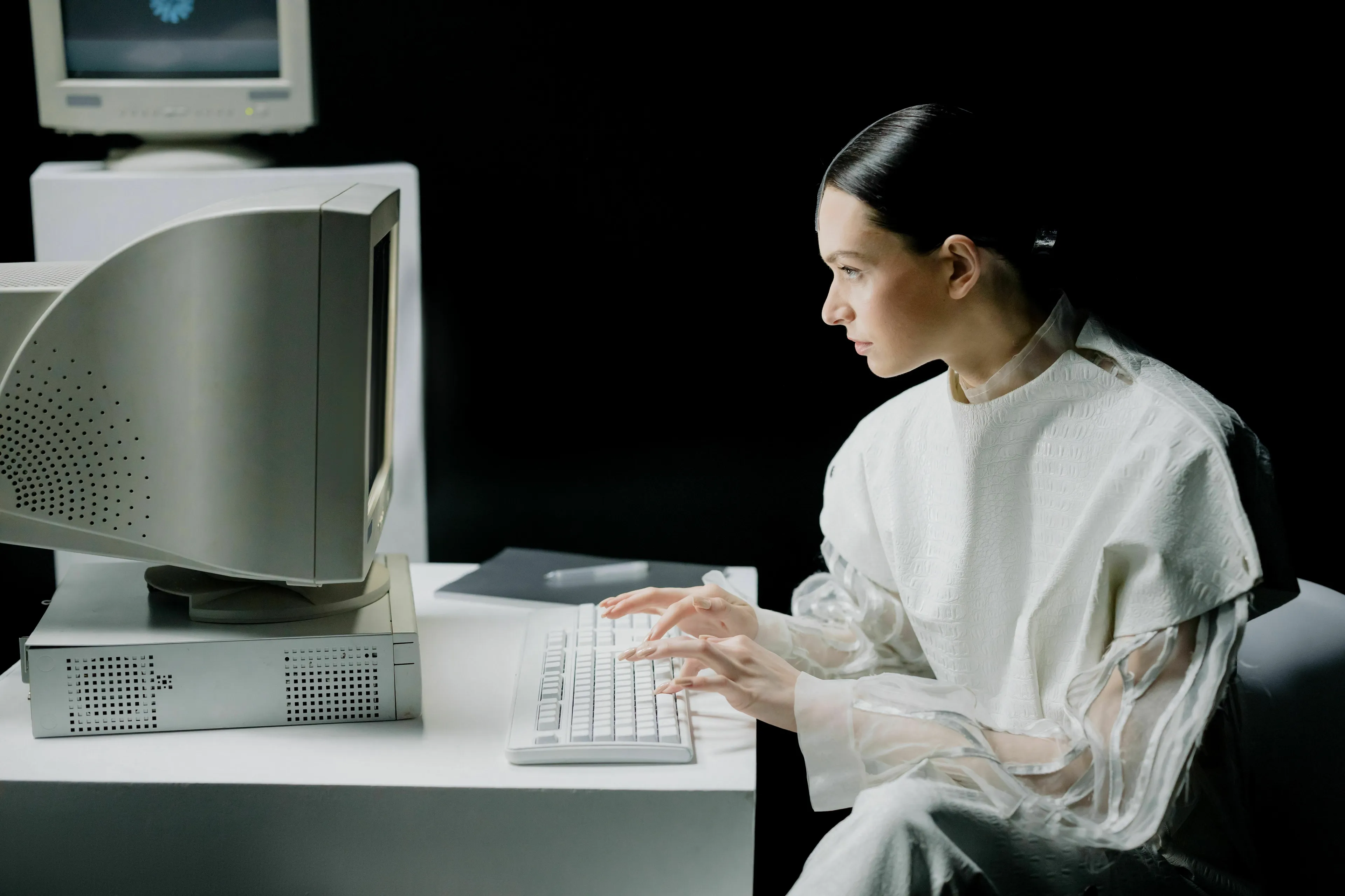 A woman sits at an old computer, typical of a general knowledge quiz setup, with a screen displaying a question.