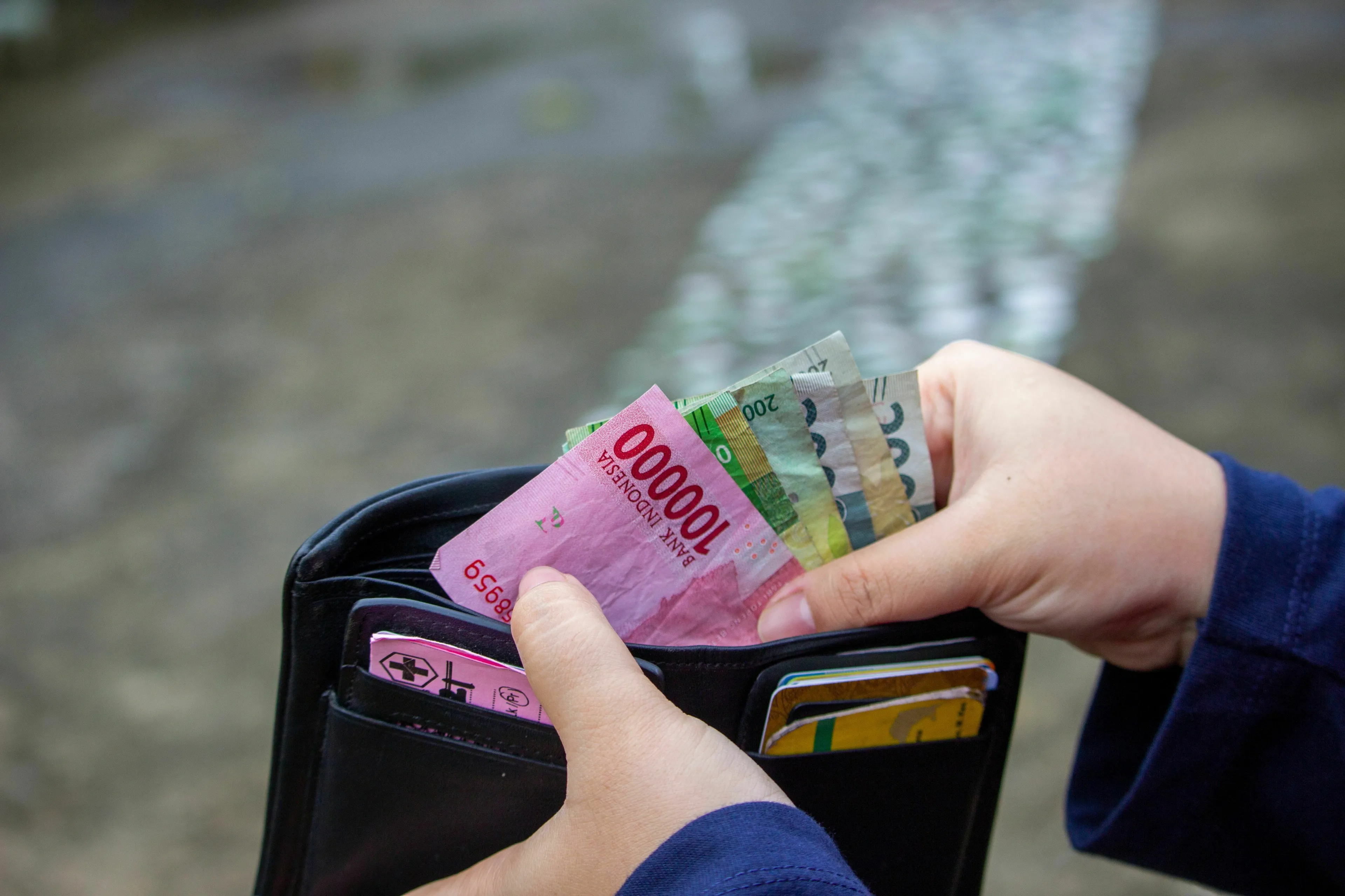 Three Letter General Knowledge Quiz: Hands holding various denominations of paper currency inside a wallet.
