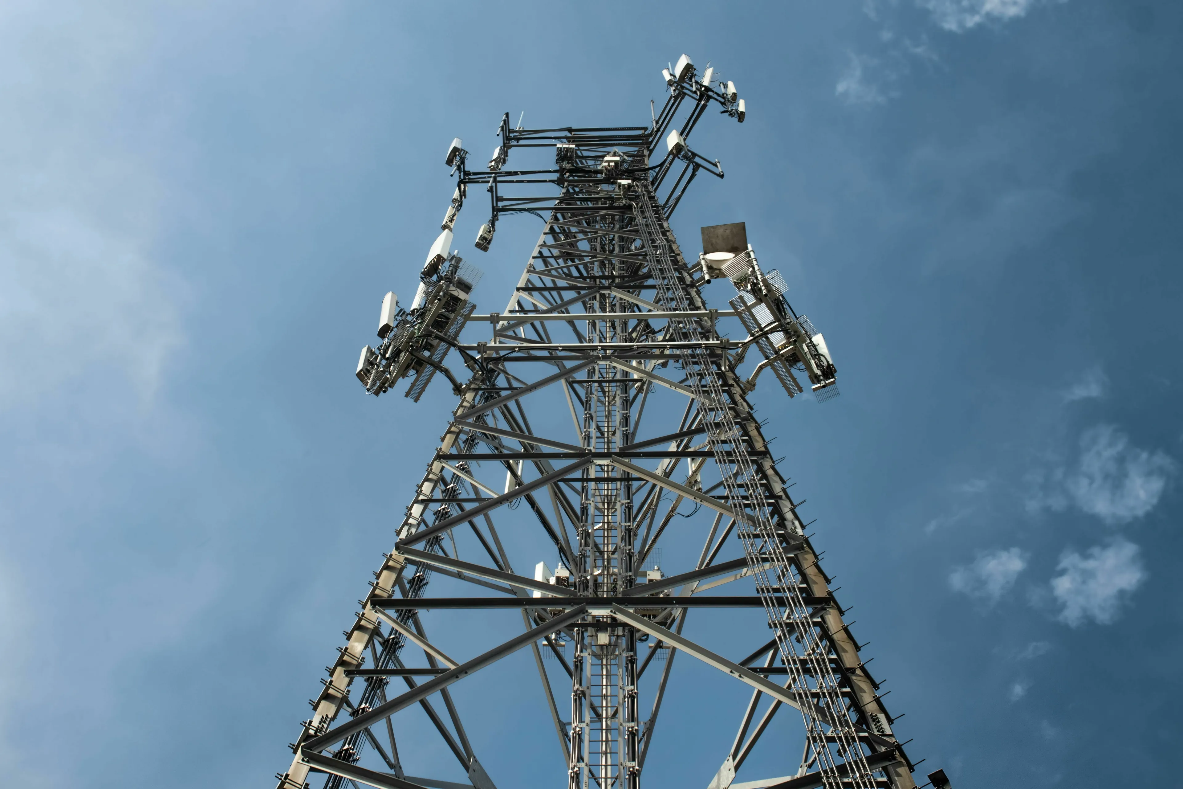 An upward view of a towering cell tower against a blue sky, prompting thoughts about its purpose and effects.