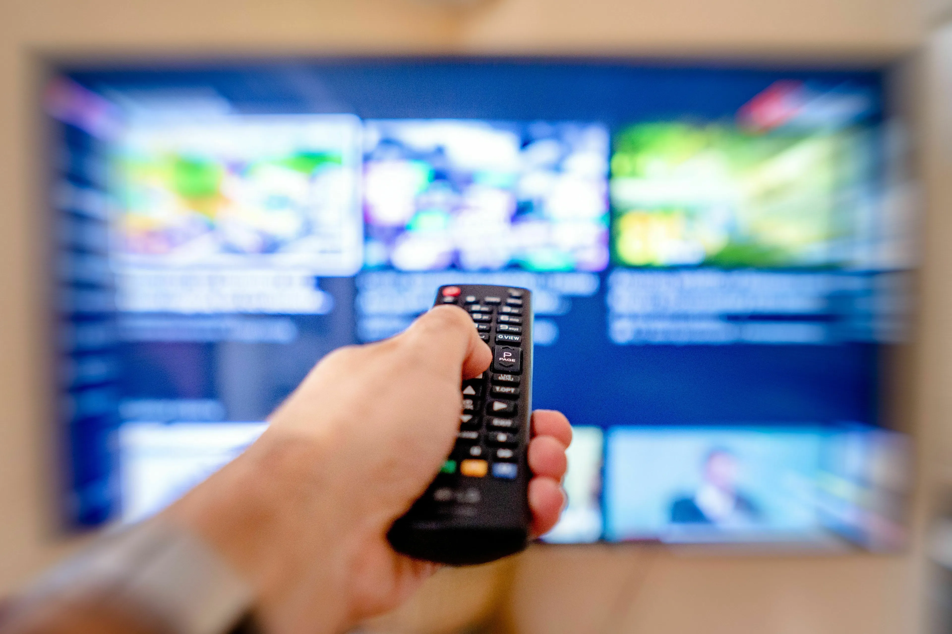 A hand holds a remote control, changing channels on a TV, reflecting an honest relationship with mainstream news.