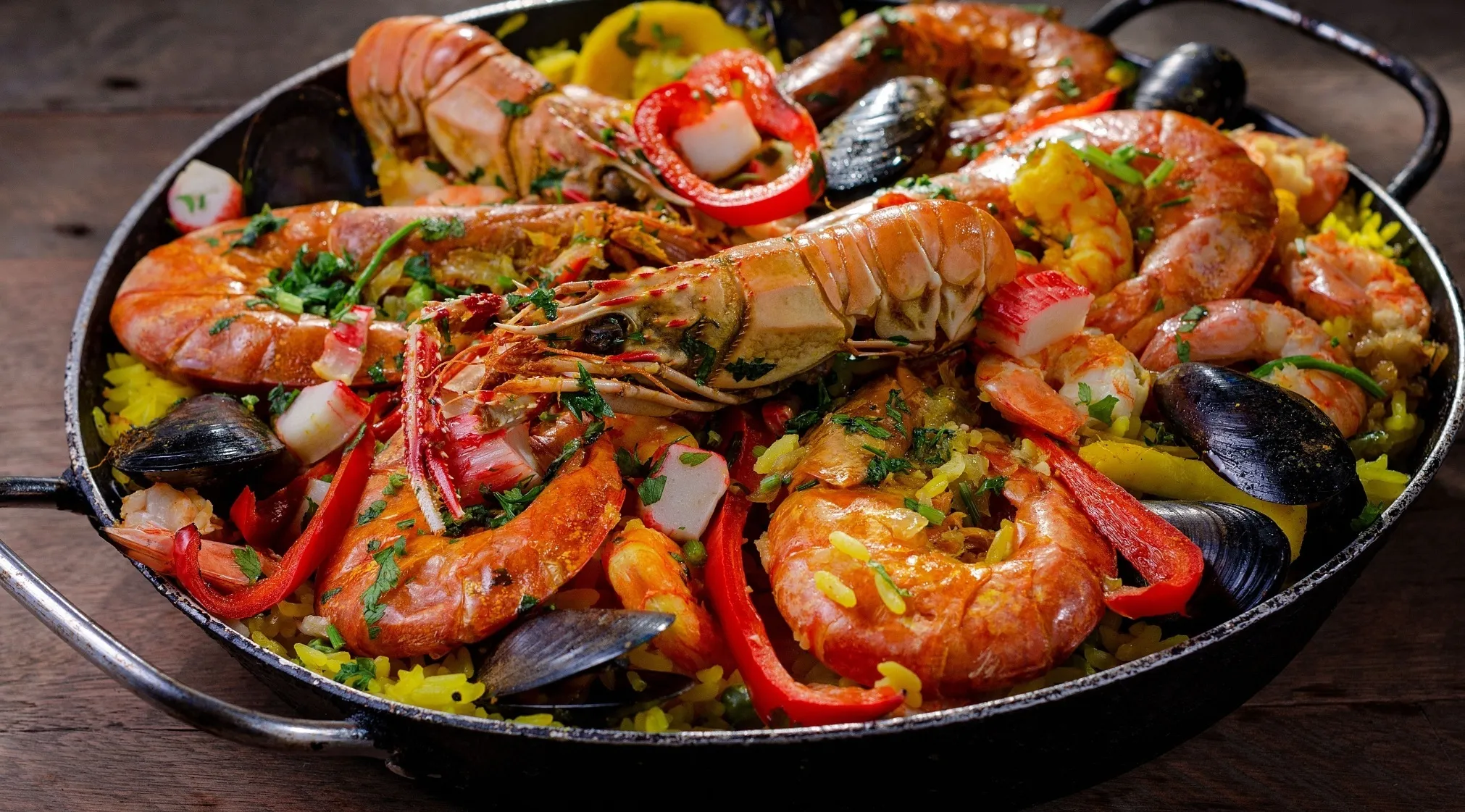 A close-up of a large pan of traditional Spanish Paella, brimming with seafood, red peppers, and yellow rice. A General Knowledge on Europe.