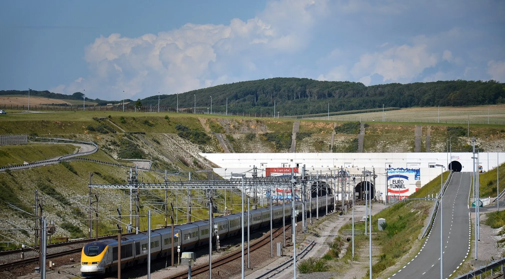An image of a Eurotunnel train in Europe, entering the Eurotunnel with a blue sky and hills in the background.
