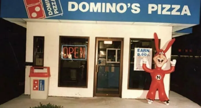 A Domino's Pizza storefront with a red Noid mascot, a throwback meme for 90s kids.