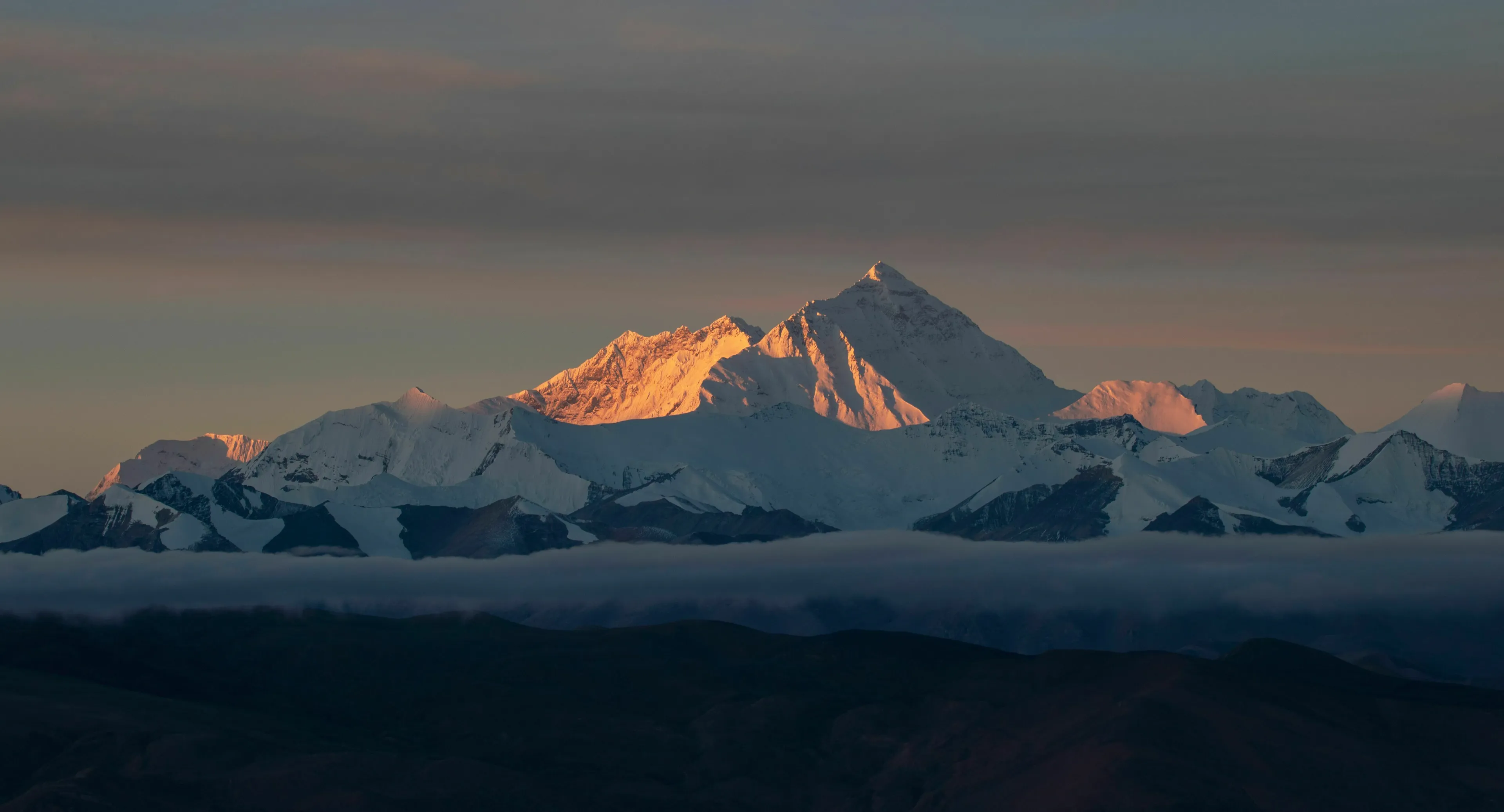 Majestic Mount Everest at sunrise, its snow-capped peaks glowing golden above a sea of clouds.