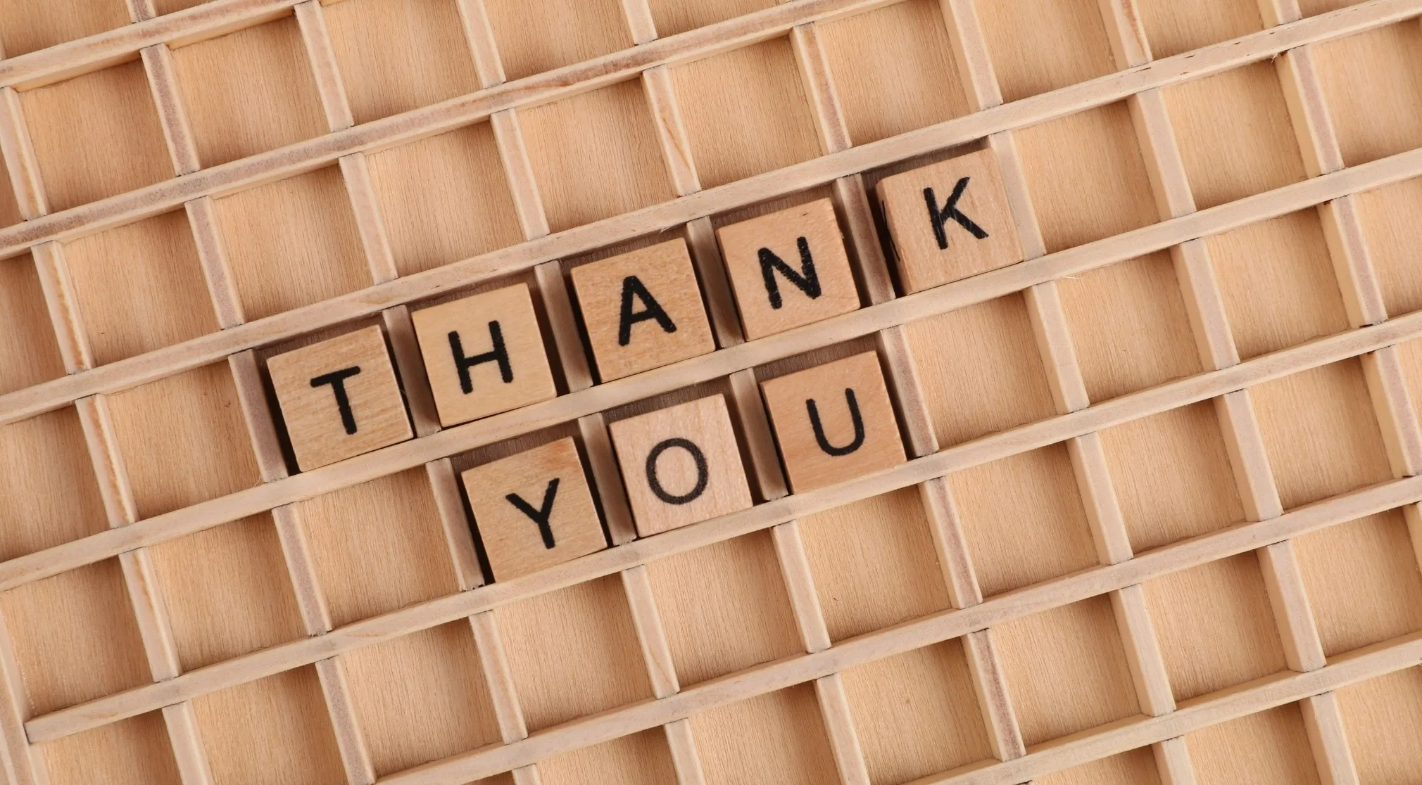 Wooden scrabble tiles spelling "THANK YOU" on a grid, for spelling bee, correcting spelling.