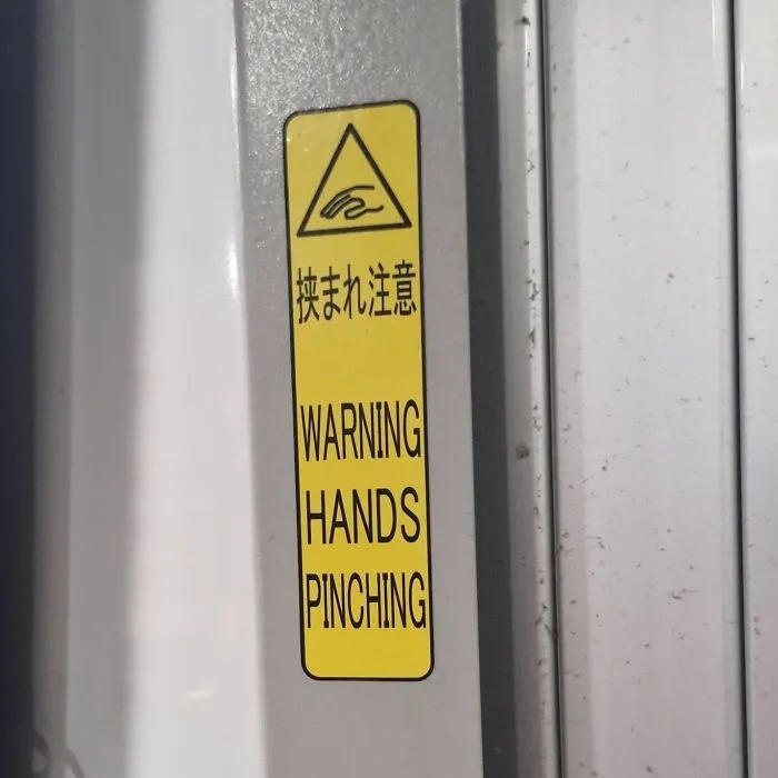 A yellow warning sticker in Japan that says WARNING HANDS PINCHING, a hilarious example of getting lost in translation.